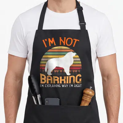 Pyrenean mountain dog apron - White dog silhouette against retro striped sun with sarcastic barking quote — shown on a black cotton canvas apron against a white background