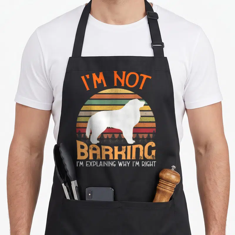 Pyrenean mountain dog apron - White dog silhouette against retro striped sun with sarcastic barking quote — shown on a black cotton canvas apron against a white background
