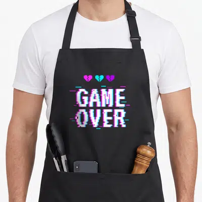 Vaporwave goth apron - Pixelated GAME OVER text with three broken hearts in pink, cyan, and purple glitch style — shown on a black cotton canvas apron against a white background