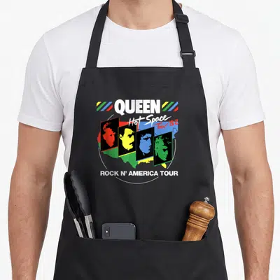 Hot queen apron - QUEEN Hot Space Tour 82 band profiles in colored rectangles over USA map — shown on a black cotton canvas apron against a white background