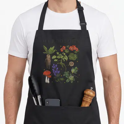 Herbology textbook plant apron - Seven numbered botanical illustrations including Mandrake and Leaping Toadstools — shown on a black cotton canvas apron against a white background