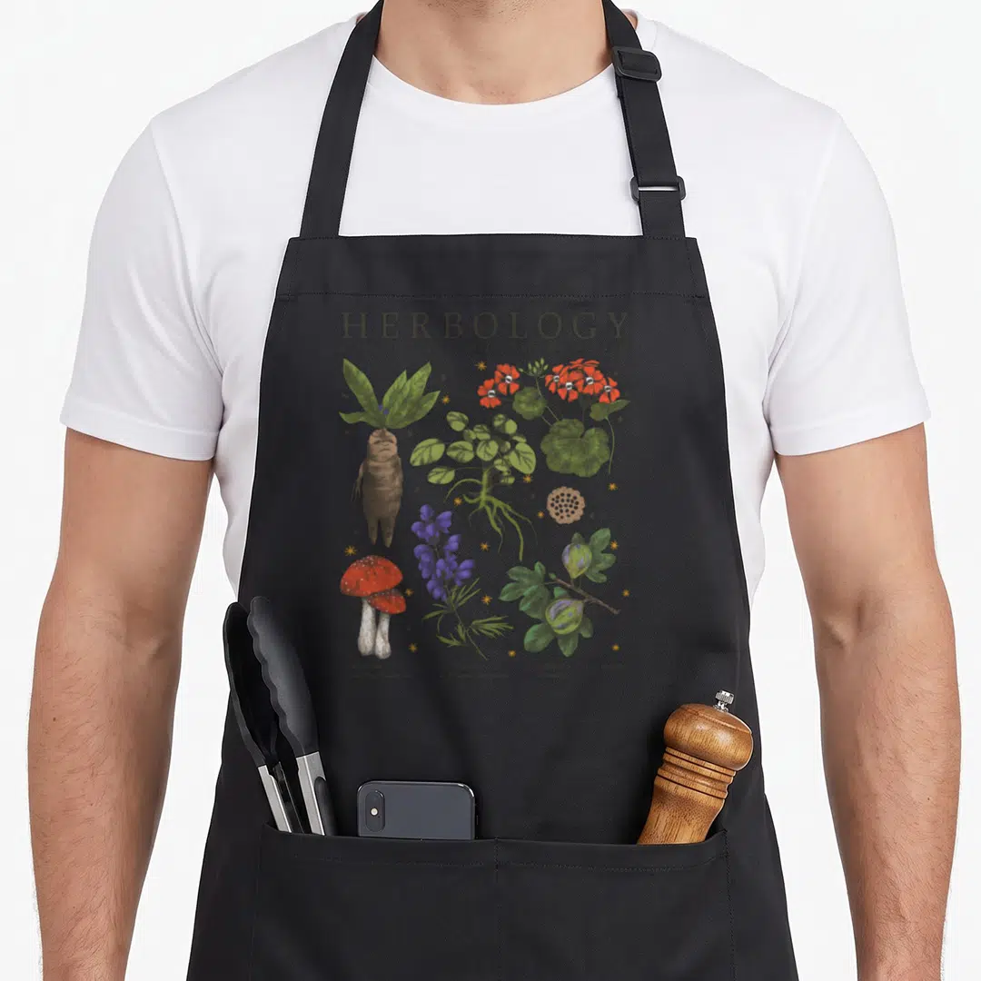 Herbology textbook plant apron - Seven numbered botanical illustrations including Mandrake and Leaping Toadstools — shown on a black cotton canvas apron against a white background