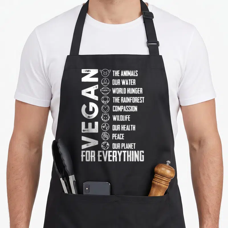 Vegan bee aprons - Vertical VEGAN text with nine icons and phrases about animals, hunger, and planet health — shown on a black cotton canvas apron against a white background