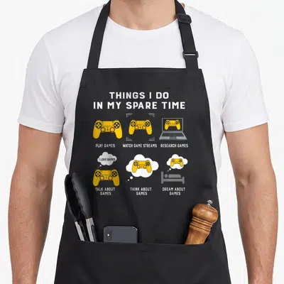 Spare gaming apron - Grey apron with yellow controller icons and text listing six gaming activities — shown on a black cotton canvas apron against a white background