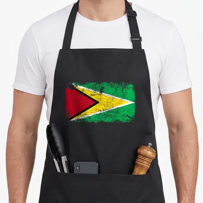 Funny flag guyana apron - Distressed rectangular flag with green yellow red and black arrow pointing right — shown on a black cotton canvas apron against a white background