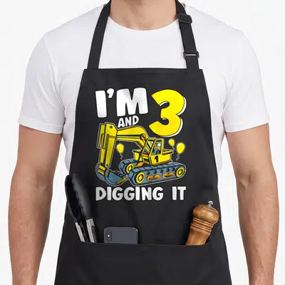 Excavator birthday apron - I'M 3 AND DIGGING IT text with yellow excavator and balloons — shown on a black cotton canvas apron against a white background