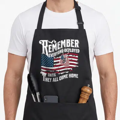 Our military apron - Distressed USA flag with dog tags and birds under text REMEMBER EVERYONE DEPLOYED UNTIL THEY ALL — shown on a black cotton canvas apron against a white background