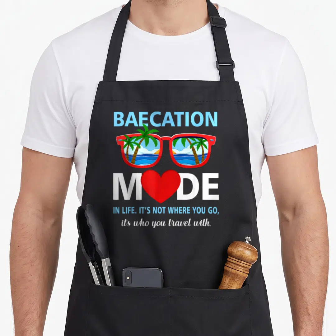Trip couple apron - Baecation Mode text with red sunglasses showing palm trees and ocean waves — shown on a black cotton canvas apron against a white background