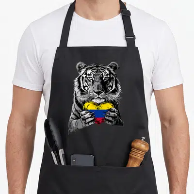 Tiger pride apron - Realistic tiger holding a heart-shaped Colombian flag in yellow blue and red — shown on a black cotton canvas apron against a white background