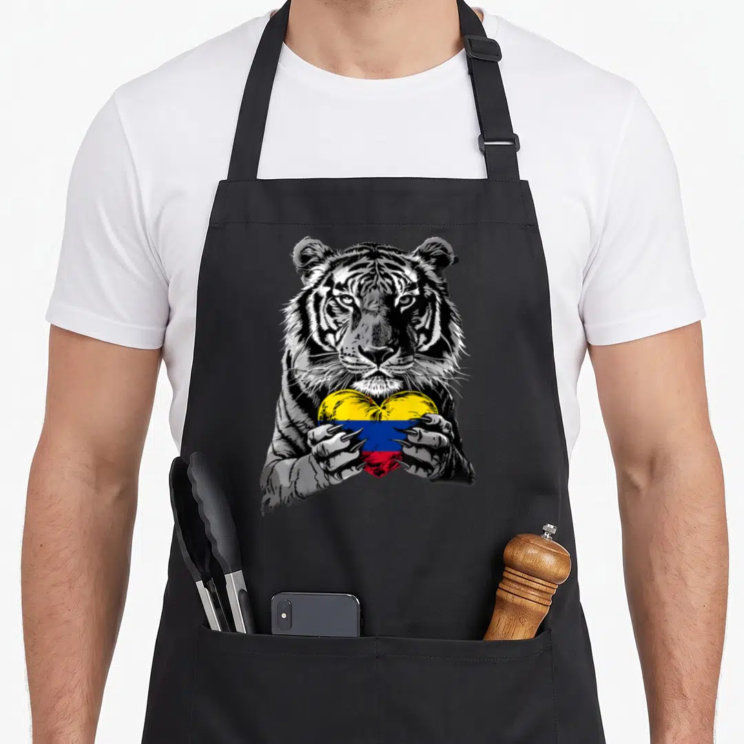 Tiger pride apron - Realistic tiger holding a heart-shaped Colombian flag in yellow blue and red — shown on a black cotton canvas apron against a white background