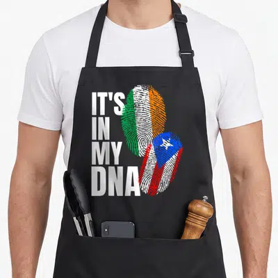 Puerto irish aprons - Stacked IT'S IN MY DNA text next to two fingerprint flags in Irish and Puerto Rican colors — shown on a black cotton canvas apron against a white background
