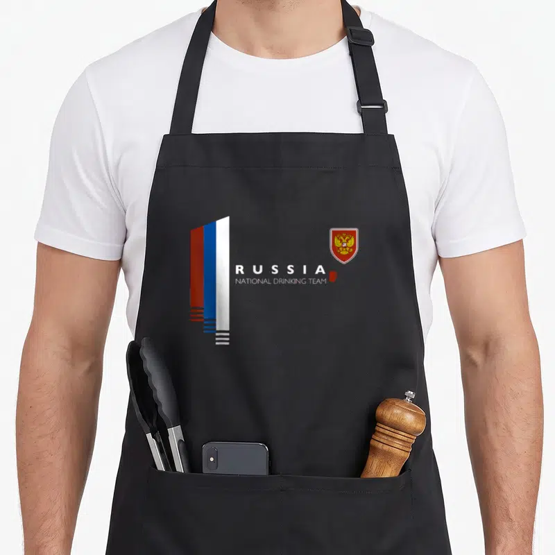 National russian apron - Russia flag stripes, drinking team text, mug, and coat of arms — shown on a black cotton canvas apron against a white background