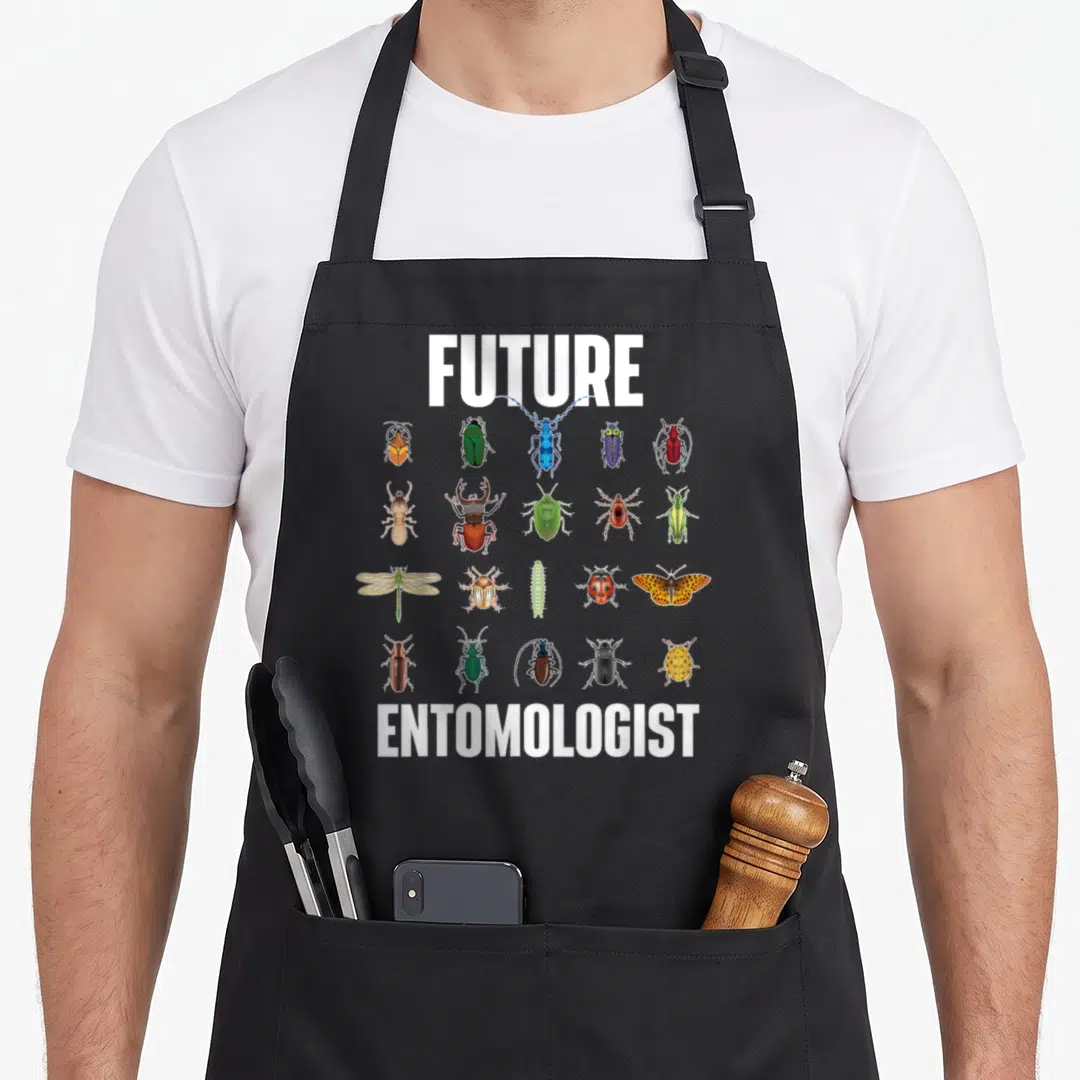 Future entomologist apron - FUTURE and ENTOMOLOGIST text framing a grid of twenty colorful realistic beetles — shown on a black cotton canvas apron against a white background