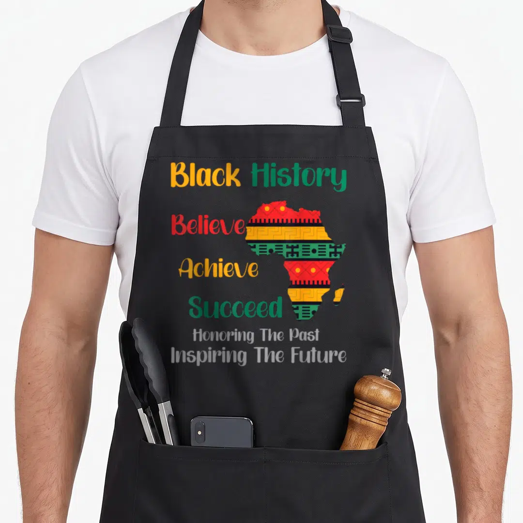 Honoring future it apron - Map of Africa with geometric patterns and stacked text reading Black History Believe Achieve — shown on a black cotton canvas apron against a white background