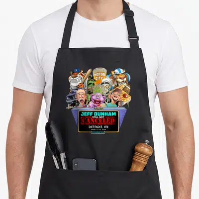 Jeff detroit apron - Caricatures above blue red sign reading Jeff Dunham Still Not Canceled Detroit 2024 — shown on a black cotton canvas apron against a white background