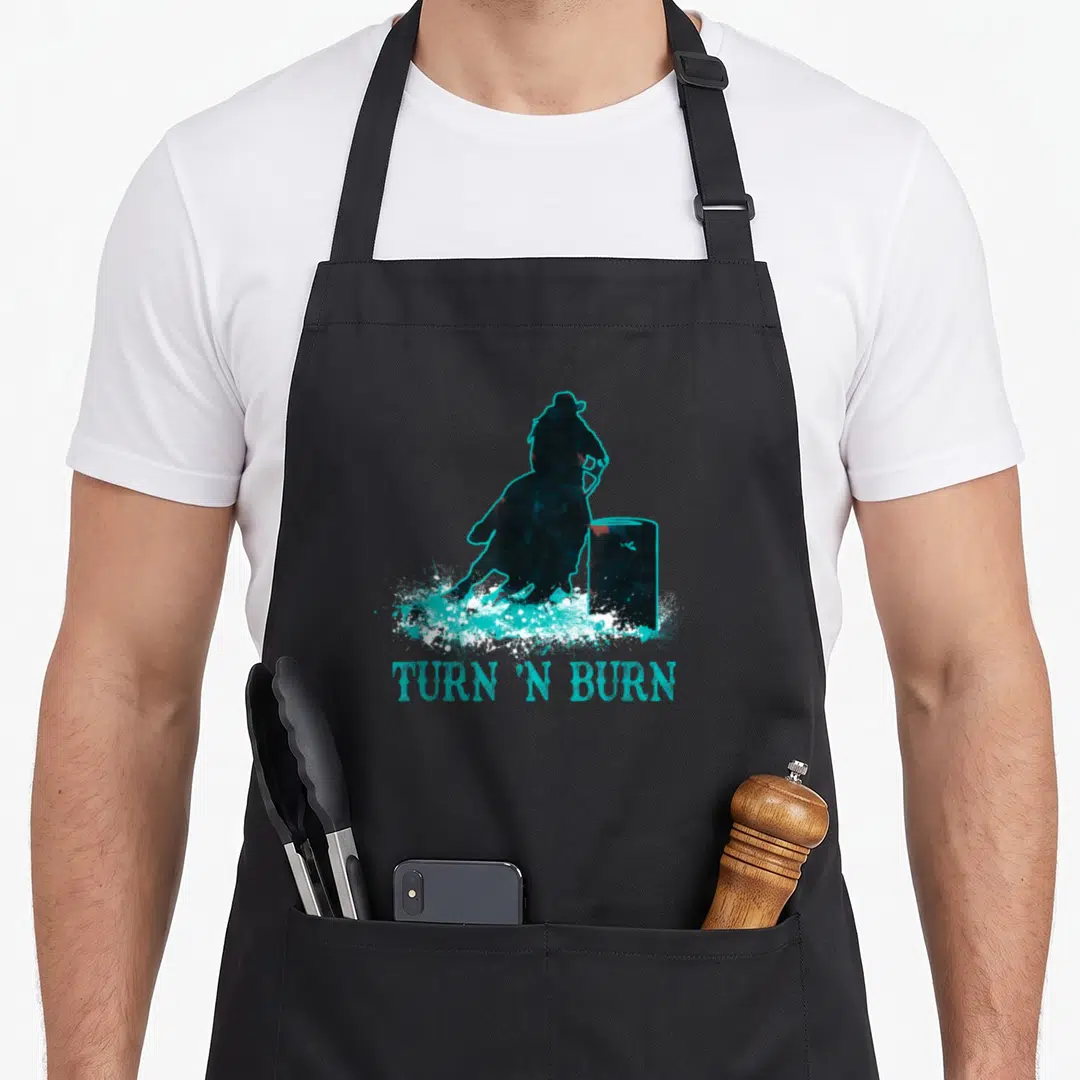 Barrel western apron - Distressed blue silhouette of horse turning barrel with cyan splatter and TURN N BURN text below — shown on a black cotton canvas apron against a white background