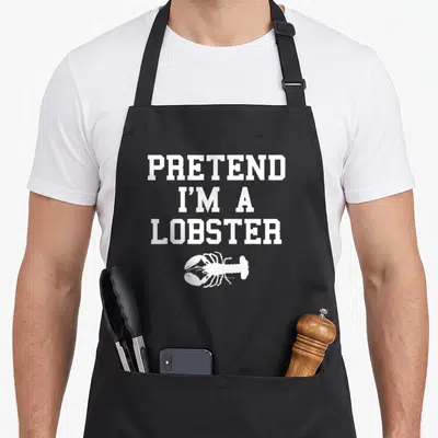 Pretend lobster apron - White PRETEND I'M A LOBSTER text stacked above a cartoon lobster illustration — shown on a black cotton canvas apron against a white background