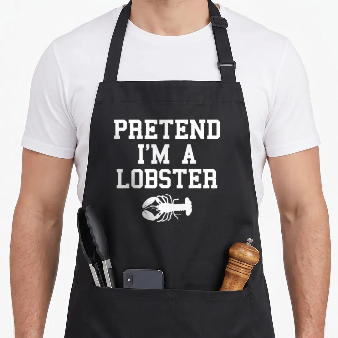 Pretend lobster apron - White PRETEND I'M A LOBSTER text stacked above a cartoon lobster illustration — shown on a black cotton canvas apron against a white background