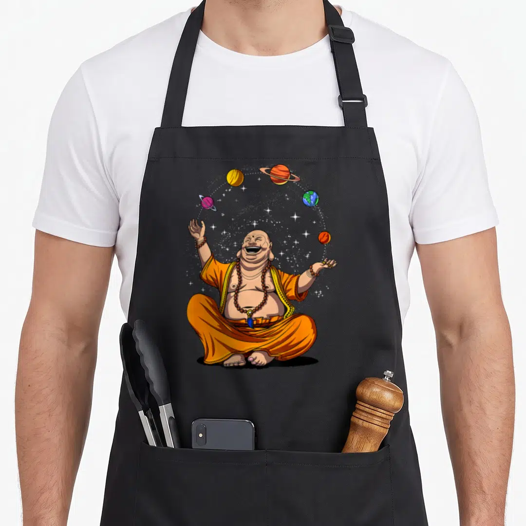 Buddha juggling apron - Seated laughing buddha in orange robes juggling five planets and stars in cartoon style — shown on a black cotton canvas apron against a white background