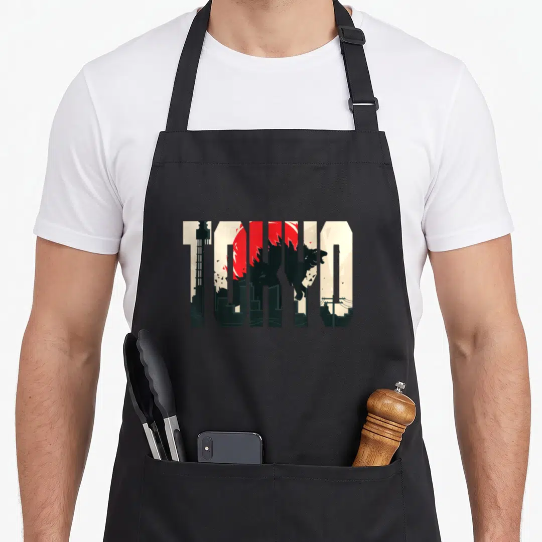 Tokyo japan apron - TOKYO text filled with city tower red sun and gorilla silhouette in beige black and red — shown on a black cotton canvas apron against a white background