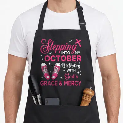 Stepping shoe apron - Pink sneakers and Stepping Into My October Birthday With God's Grace And Mercy text with stars — shown on a black cotton canvas apron against a white background