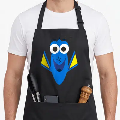 Dory face apron - Blue cartoon fish with yellow fins and big white eyes facing forward — shown on a black cotton canvas apron against a white background