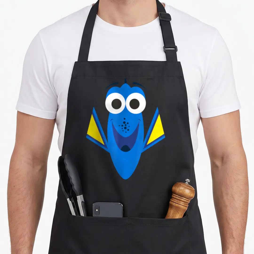 Dory face apron - Blue cartoon fish with yellow fins and big white eyes facing forward — shown on a black cotton canvas apron against a white background