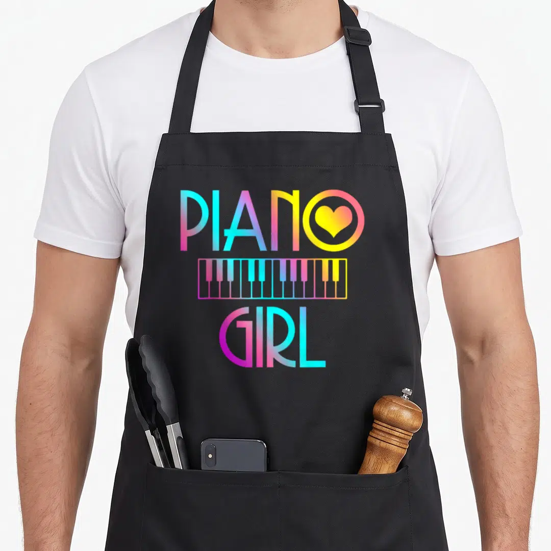 Musical piano apron - Gradient PIANO GIRL text with heart in O and keyboard strip in cyan magenta yellow — shown on a black cotton canvas apron against a white background