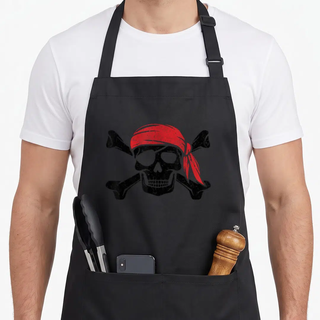Pirate crossbone skull apron - Distressed skull wearing red bandana over two crossed black bones — shown on a black cotton canvas apron against a white background