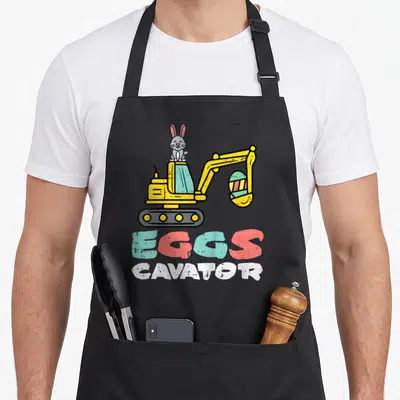 Cavator easter egg apron - Grey bunny on yellow excavator holding striped egg with EGGS CAVATOR text — shown on a black cotton canvas apron against a white background