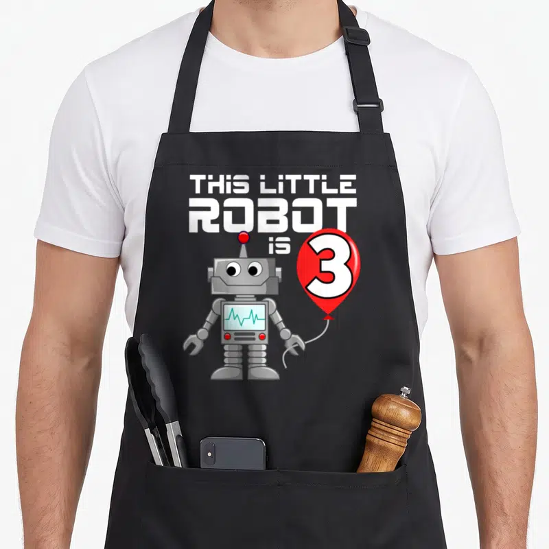 Robot science apron - THIS LITTLE ROBOT is 3 text above grey cartoon robot holding red balloon with teal screen — shown on a black cotton canvas apron against a white background