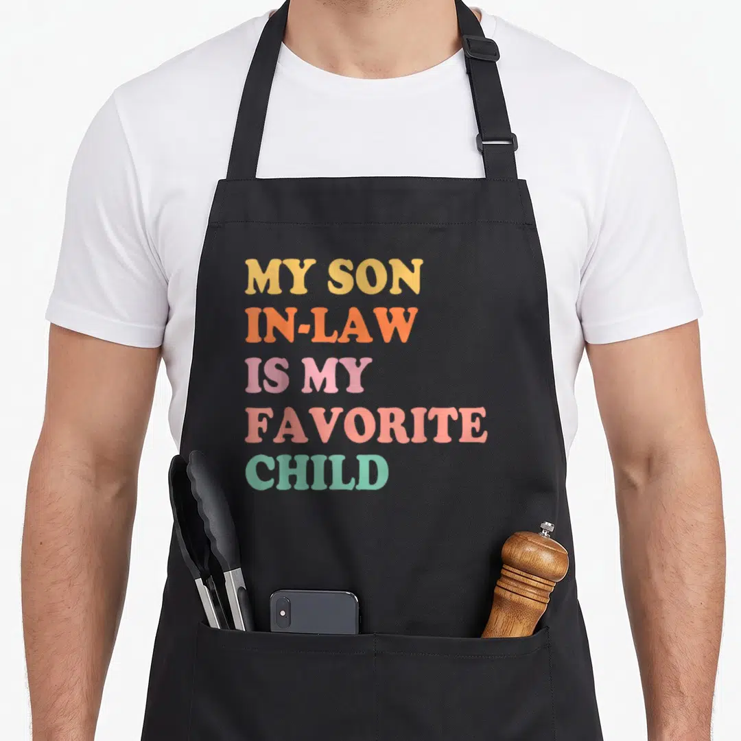Son law mother's day aprons - Stacked text reading my son in law is my favorite child in pastel rainbow colors — shown on a black cotton canvas apron against a white background