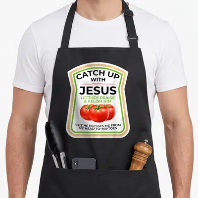 Psalm catch up with jesus apron - Ketchup label design with three red tomatoes and text CATCH UP WITH JESUS PSALM 37:4 — shown on a black cotton canvas apron against a white background