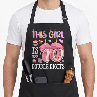 10th double digit birthday apron - Cupcake number 10 with balloons and THIS GIRL IS NOW DOUBLE DIGITS text — shown on a black cotton canvas apron against a white background