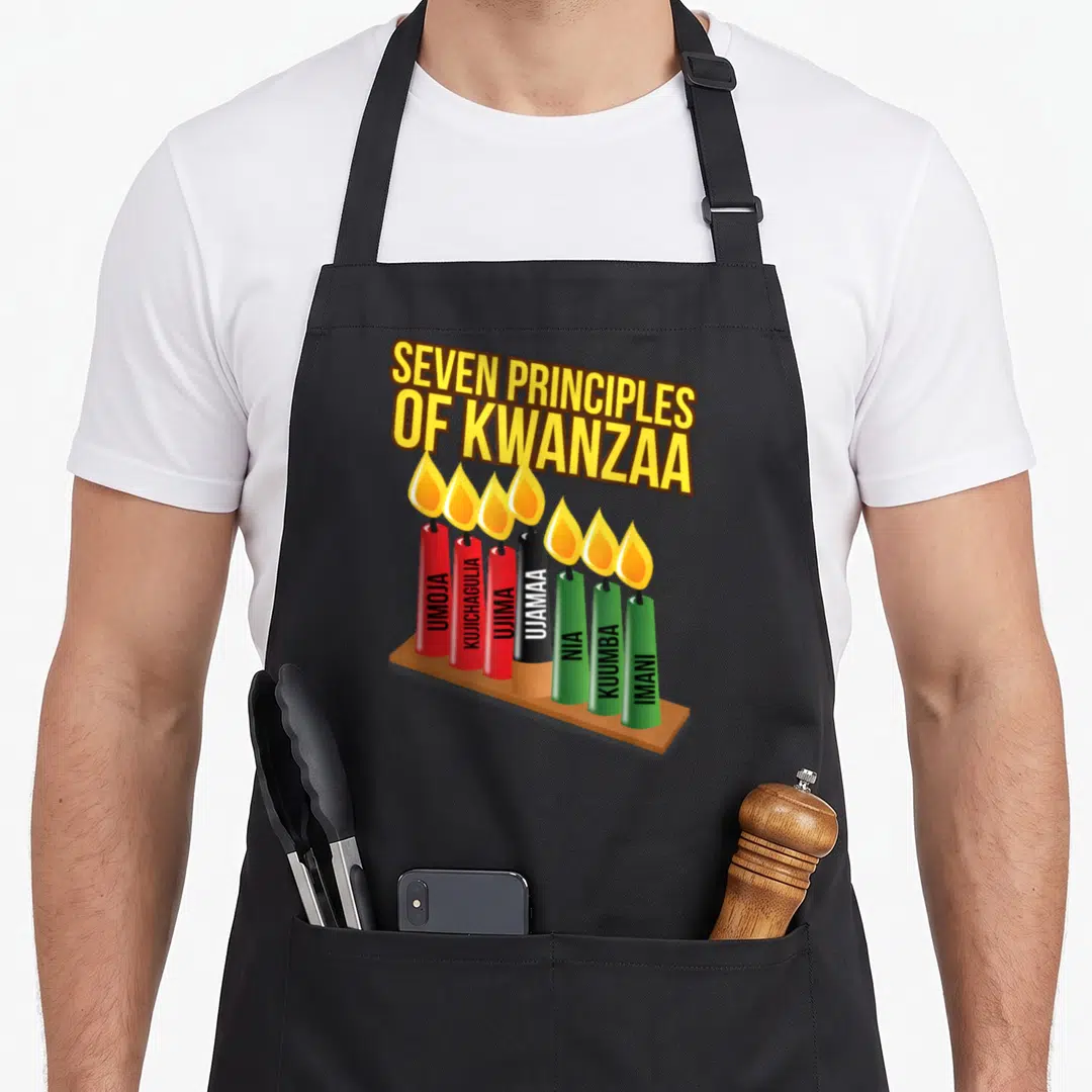 Seven funny kwanzaa apron - Seven Principles of Kwanzaa text above red black and green kinara candles with vertical — shown on a black cotton canvas apron against a white background