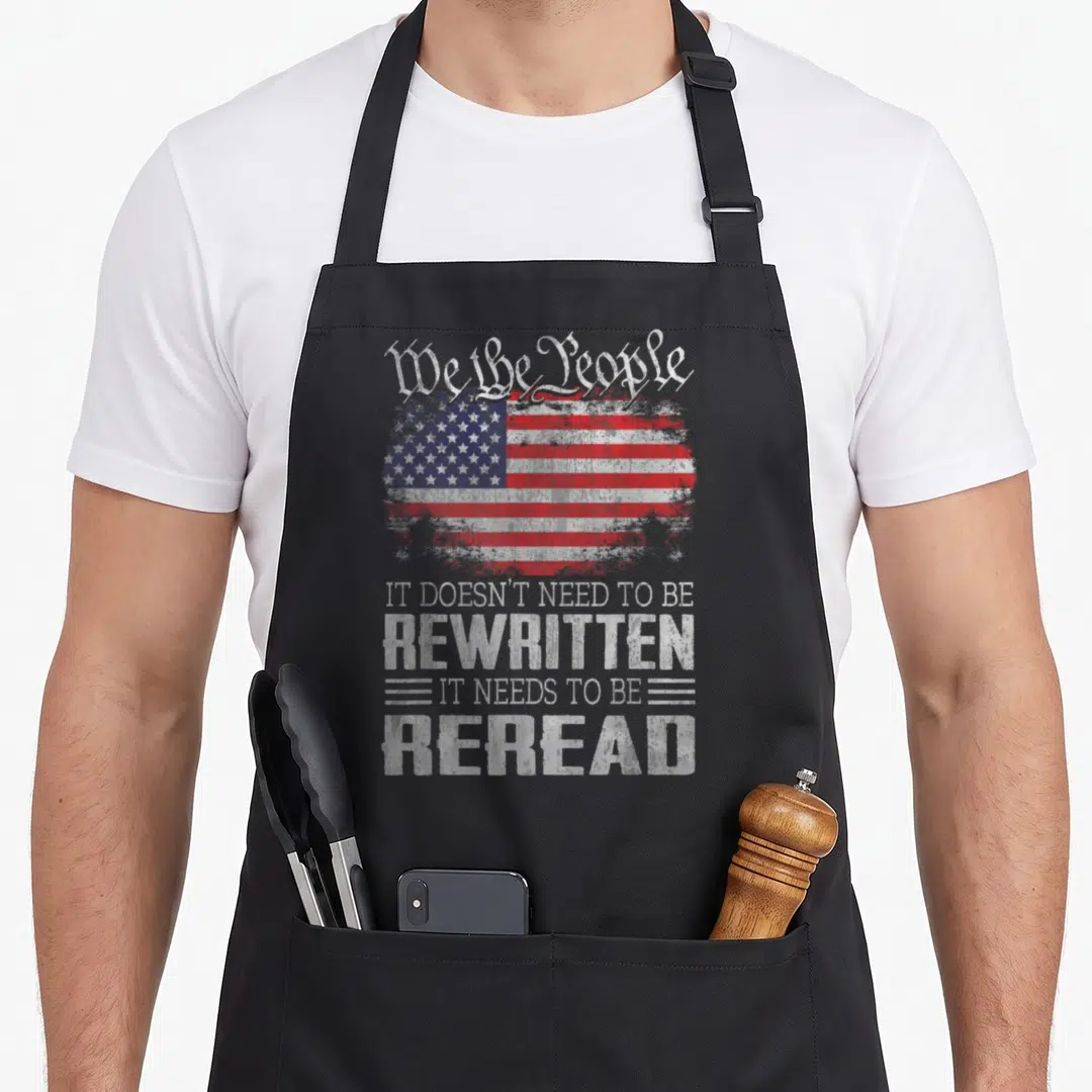 Flag us aprons - Distressed USA flag with We the People text and reread message in white red blue — shown on a black cotton canvas apron against a white background