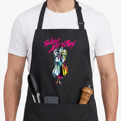 Villain cruller apron - Pink Slay All Day text above cartoon woman in spotted coat with yellow and blue accents — shown on a black cotton canvas apron against a white background