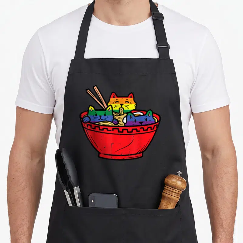 Ramen gay pride apron - Three rainbow cats in red ramen bowl with yellow noodles and chopsticks — shown on a black cotton canvas apron against a white background