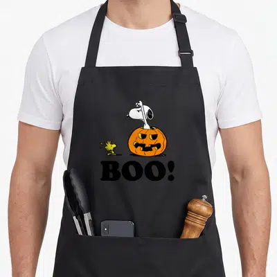 Woodstock boo halloween apron - Snoopy inside orange pumpkin with Woodstock and black BOO text — shown on a black cotton canvas apron against a white background