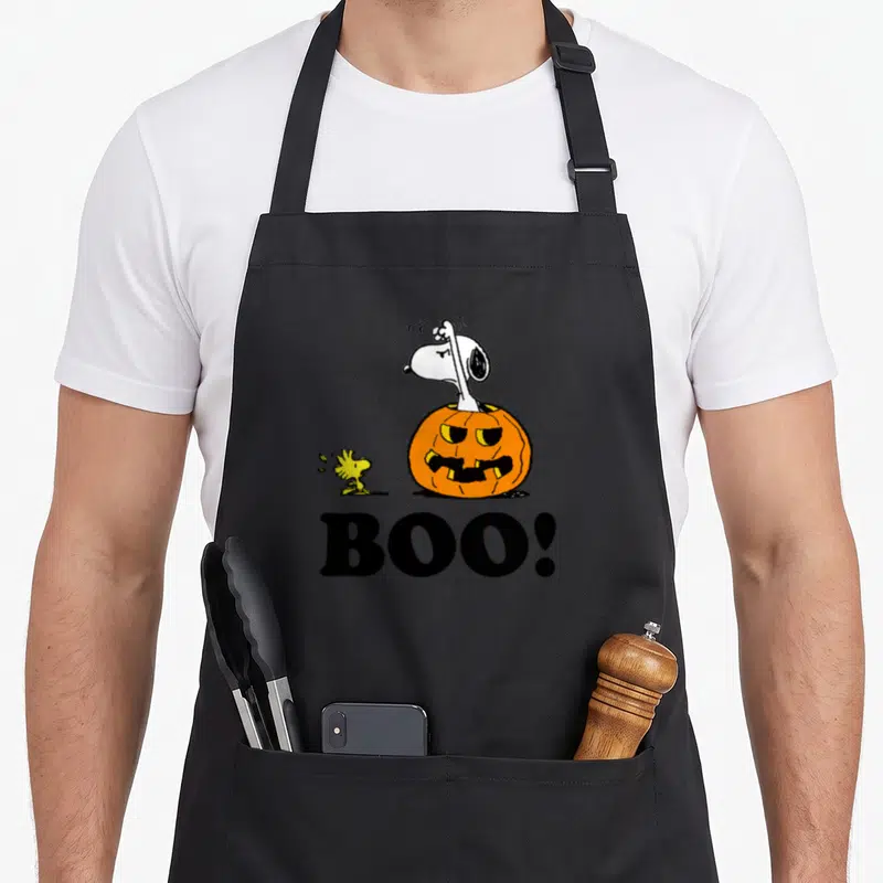 Woodstock boo halloween apron - Snoopy inside orange pumpkin with Woodstock and black BOO text — shown on a black cotton canvas apron against a white background