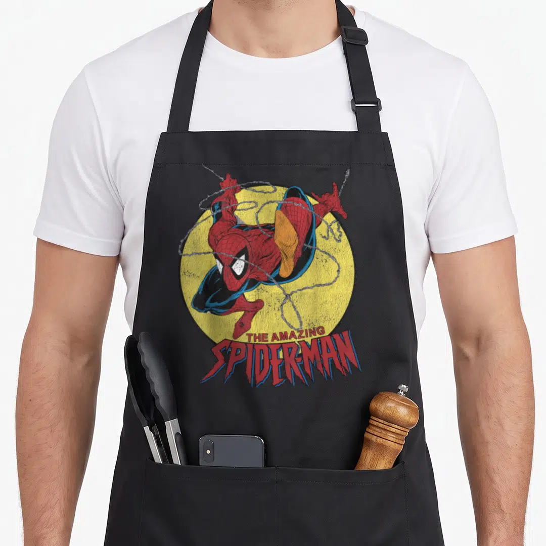 Jump amazing aprons - Spider-Man in red blue suit on yellow circle with webs and stacked logo text below — shown on a black cotton canvas apron against a white background