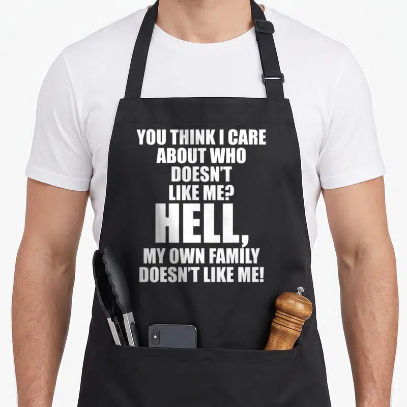 Care family aprons - White stacked text reading You Think I Care About Who Doesn't Like Me Hell My Own Family Doesn't — shown on a black cotton canvas apron against a white background
