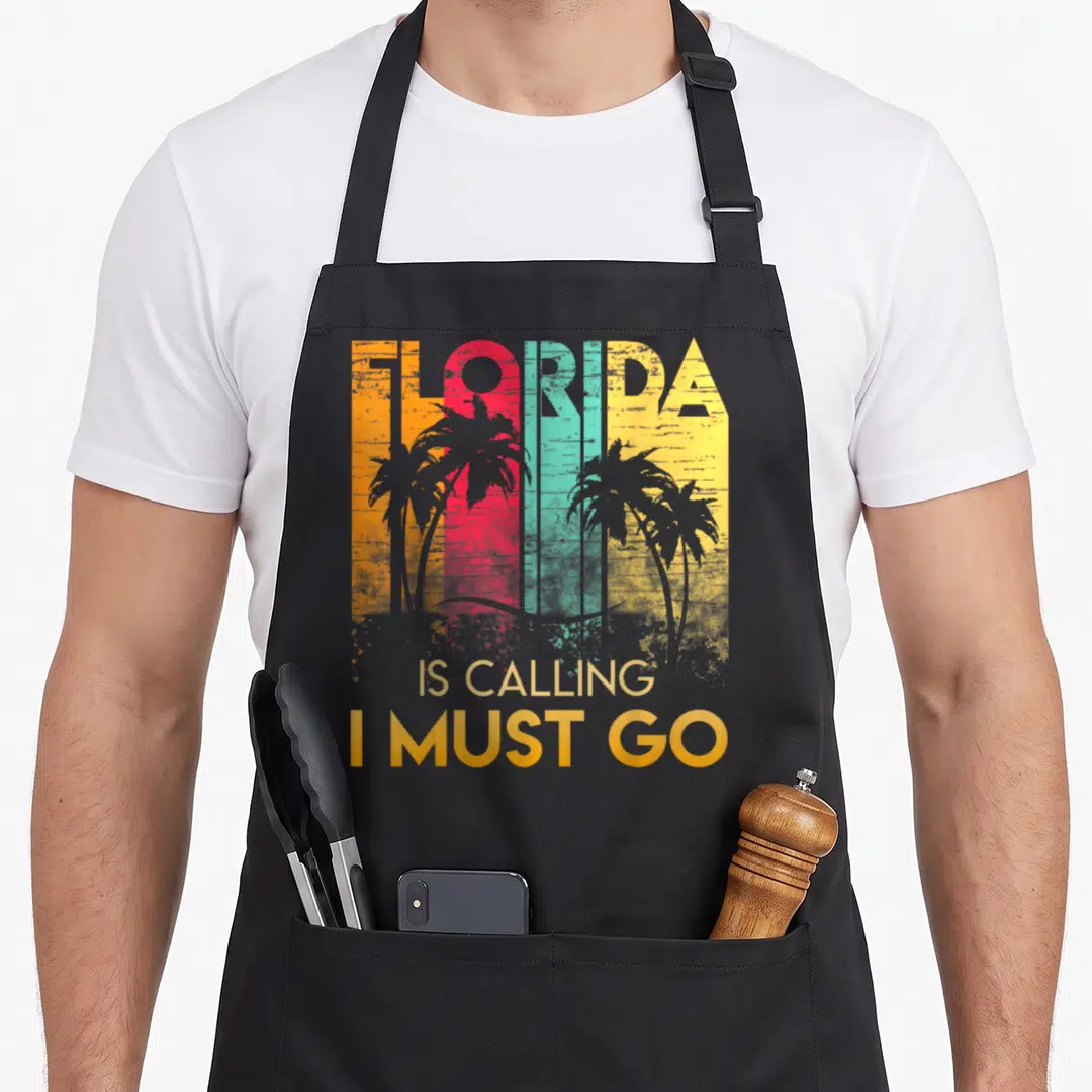 Florida summer aprons - Retro FLORIDA text in orange red teal yellow stripes with palm trees and IS CALLING I MUST GO — shown on a black cotton canvas apron against a white background
