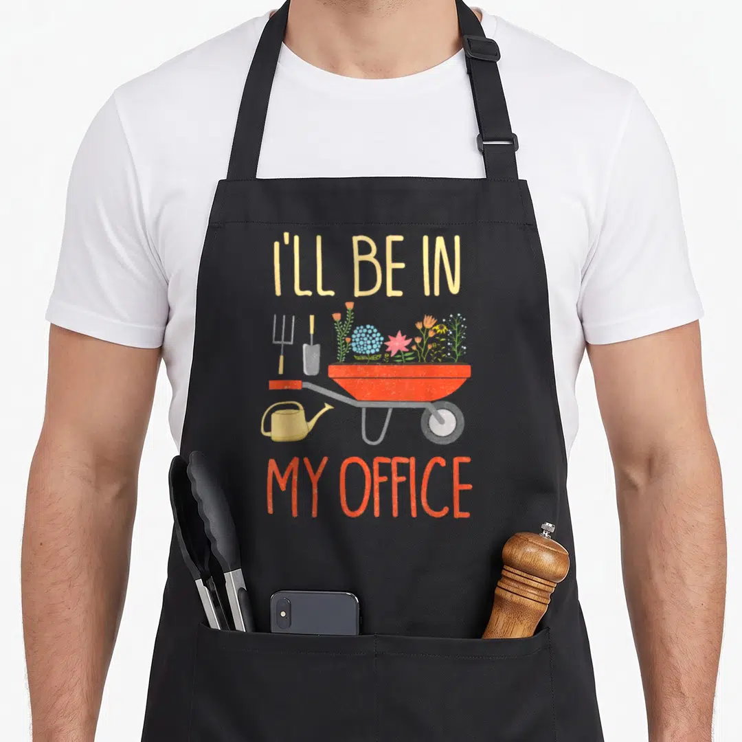 Ill office apron - Red wheelbarrow with flowers and tools below I'll be in my office text — shown on a black cotton canvas apron against a white background