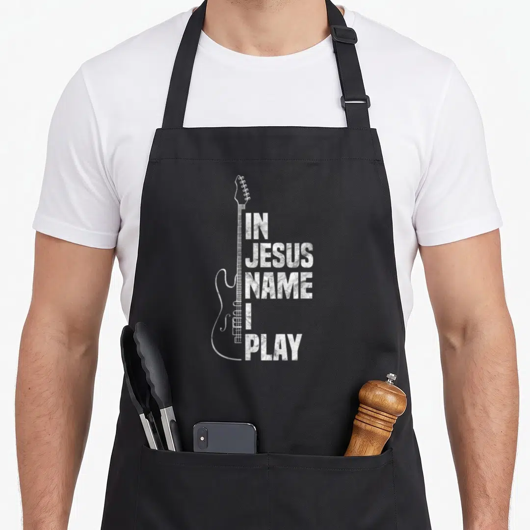 Guitar christian apron - White distressed electric guitar outline beside stacked IN JESUS NAME I PLAY text — shown on a black cotton canvas apron against a white background