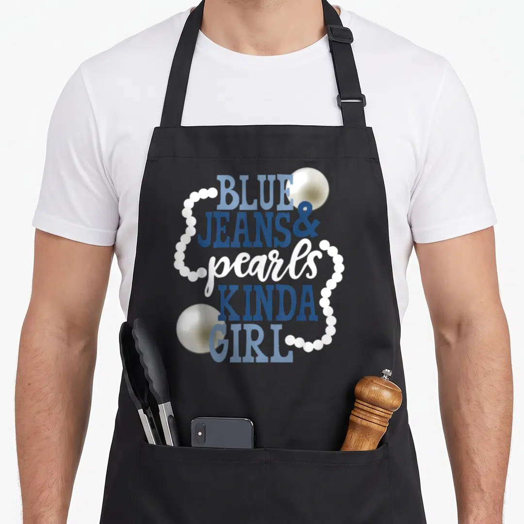 Blue jean apron - Stacked blue and white text reading Blue Jeans Pearls Kinda Girl with pearl necklace graphics — shown on a black cotton canvas apron against a white background