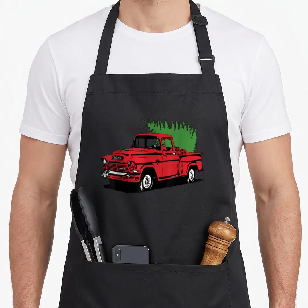 Truck holiday christmas tree apron - Red cartoon truck carrying a green Christmas tree in the bed — shown on a black cotton canvas apron against a white background