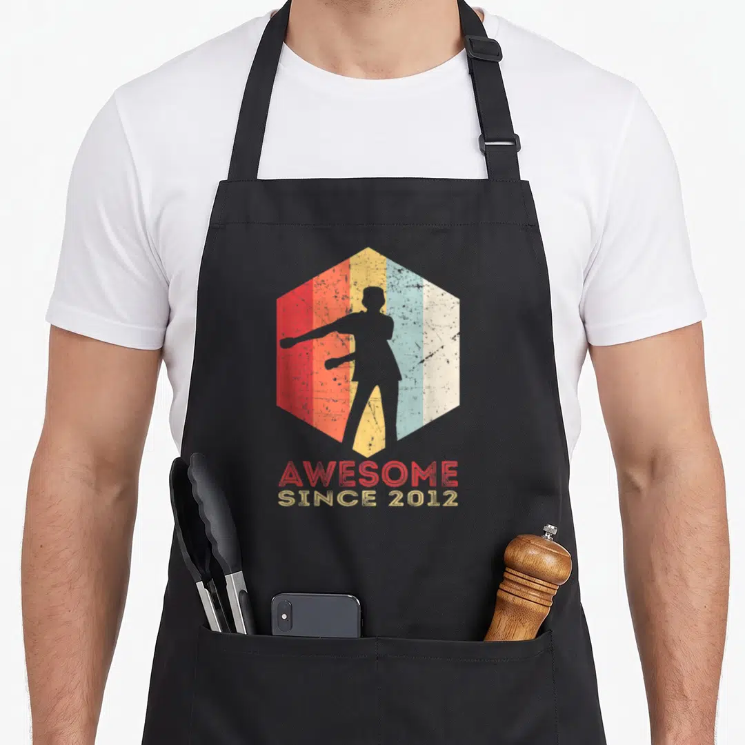 10th trendy apron - Grey person silhouette inside red orange yellow blue striped hexagon with stacked AWESOME SINCE — shown on a black cotton canvas apron against a white background