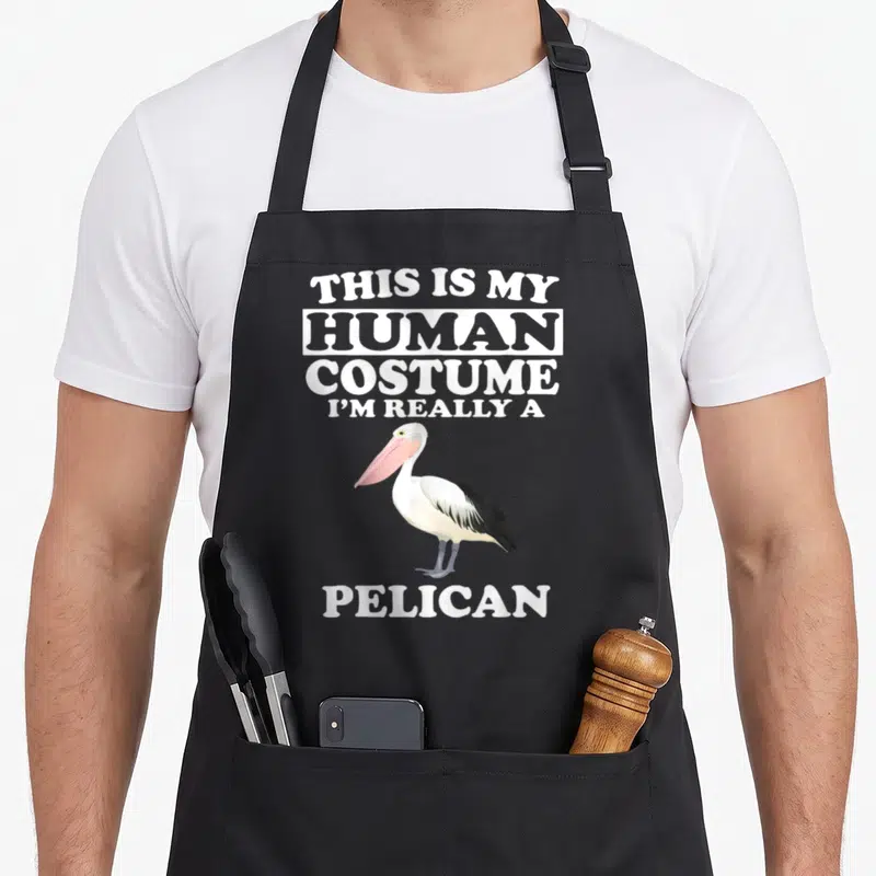 Human pelican apron - Pelican with pink bill and text This Is My Human Costume I'm Really A Pelican — shown on a black cotton canvas apron against a white background