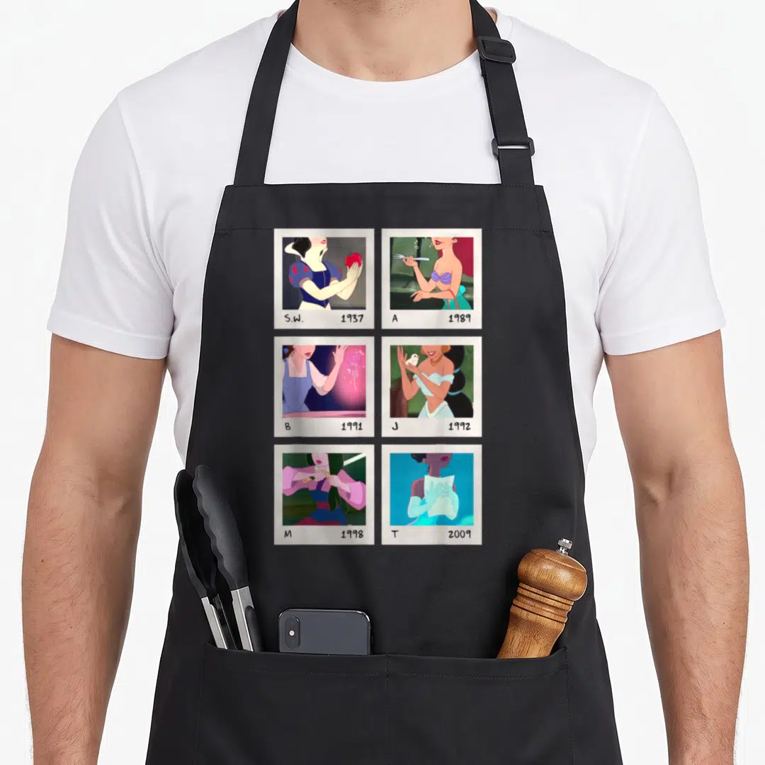 Polaroid princess apron - Six polaroid photos of princesses with initials S.W. A B J M T and years 1937-2009 — shown on a black cotton canvas apron against a white background